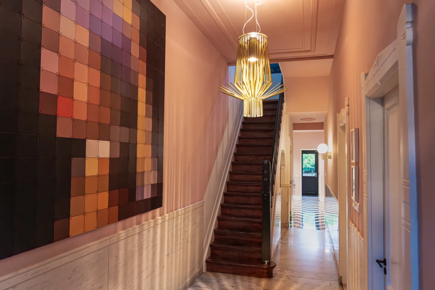 De hal van het pand, met een trap en een IXXI in bruin-oranje pixels aan de roze wand