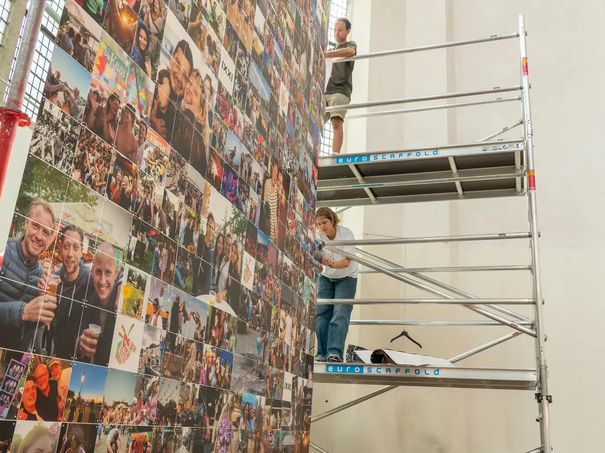 Twee mensen bouwen in een kerk een grote IXXI van honderden foto’s op